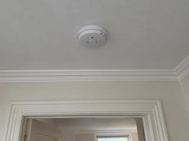 Ceiling-mounted smoke alarm above a doorway in a cream hallway with decorative trim in Freshwater